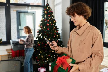 Meslektaşlar, süslemeler ve hediyelerle çevrili neşeli bir Noel toplantısının tadını çıkarıyorlar.