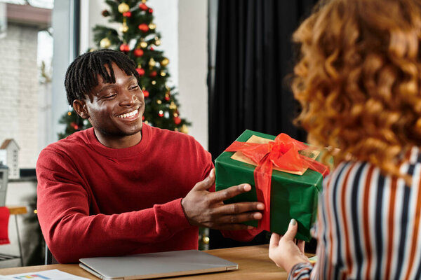 Коллеги радостно обмениваются завернутыми подарками, празднуя праздничный дух в офисе.