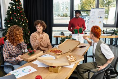 Bir grup neşeli iş arkadaşı ofislerinde hediyelerle Noel kutlaması yapıyorlar..