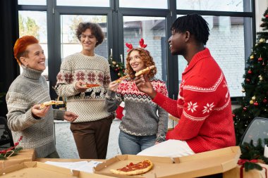 Bir grup genç iş arkadaşı iş yerindeki Noel kutlamaları sırasında kahkaha ve pizzayı paylaşıyor..