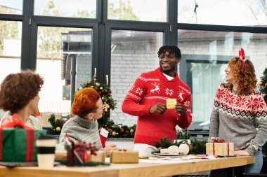 Bir grup neşeli iş arkadaşı Noel için dekore edilmiş bir ofiste bayram neşesini ve hediyeleri paylaşıyor..