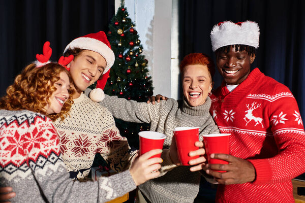 Веселая группа молодых сотрудников делится напитками во время празднования праздничного духа в офисе.