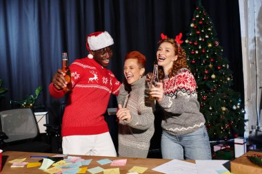 A group of cheerful coworkers share laughter and drinks while celebrating Christmas together. clipart