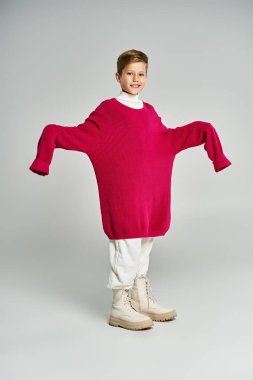 A cheerful boy wears a large pink sweater and smiles, embodying winter warmth and fun. clipart