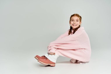Pembe kazak giyen genç bir kız otururken neşeli bir anın tadını çıkarıyor..