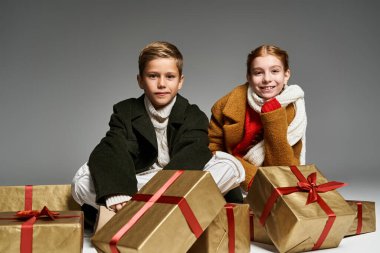 İki mutlu çocuk güzel paketlenmiş hediyelerle birlikte oturur, kış mevsiminin tadını çıkarırlar..