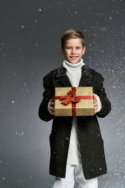 A young boy smiles brightly while showcasing a present amid softly falling snowflakes. clipart