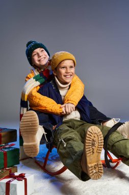 Two boys dressed in cozy winter attire smile while sledding in a festive atmosphere. clipart