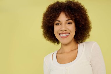 A young woman with curly hair radiates happiness while standing in her underwear against a bright yellow backdrop. clipart