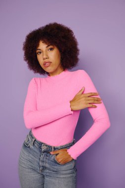 Mor bir arkaplanda duran genç bir kadın, pembe elbiselere olan güvenini ve tarzını gösteriyor..