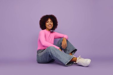 A young woman with curly hair smiles brightly, exuding joy and playfulness as she sits casually. clipart