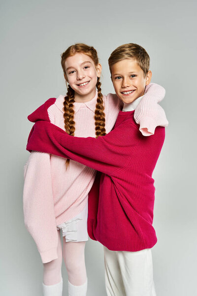 Two children share a warm embrace, showcasing their cozy winter outfits and bright smiles.