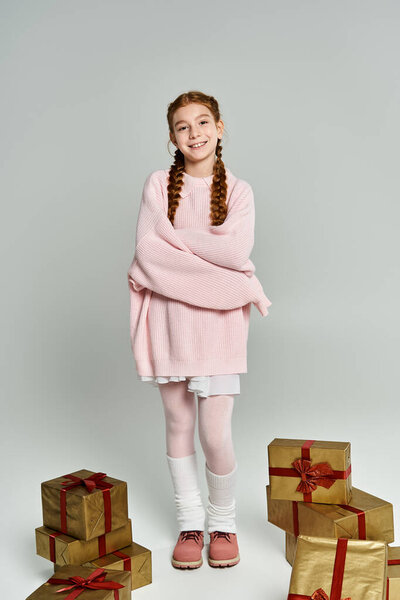 Веселая девушка одета тепло стоит среди красиво обернутых подарков в уютной обстановке.