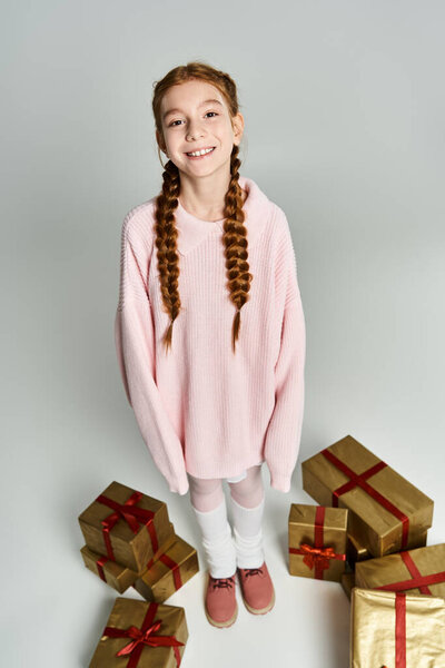 Очарованная молодая девушка в розовом свитере стоит с праздничными подарками, захватив праздничное настроение.