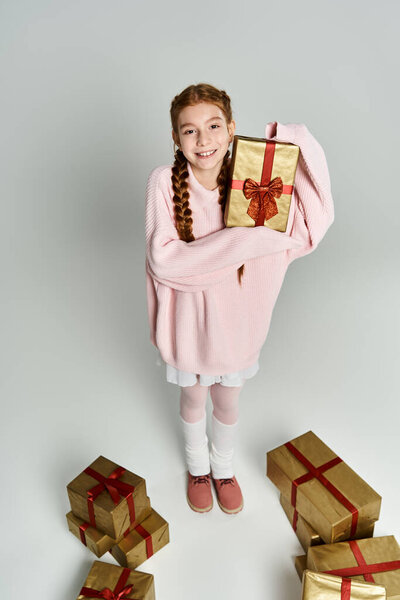 Веселая молодая девушка, одетая тепло, обнимает красиво завернутый подарок среди красочных подарков.