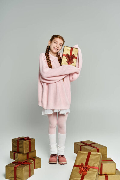 Улыбающаяся девушка в теплой одежде стоит среди подарков, излучая праздничное настроение и волнение.