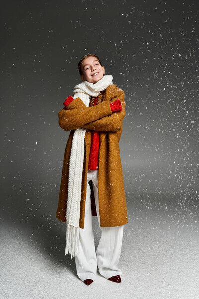 The girl stands happily in warm layers, embracing winter joy amid falling snowflakes.