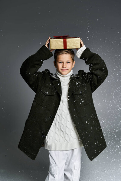 A cheerful boy dressed for winter joyfully holds a gift above his head in the snow.