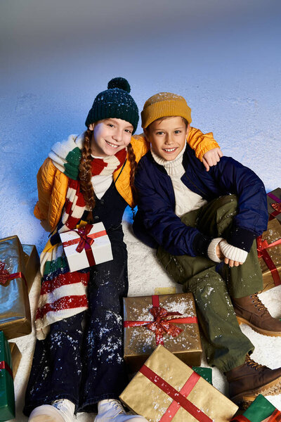Двое веселых детей, тепло одетых, празднуют зиму с улыбками и подарками.