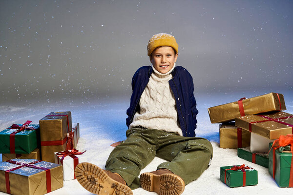 Радостный мальчик сидит в снегу с красивыми завернутыми подарками, обнимая волшебство зимы.