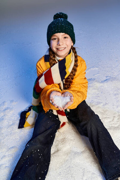 Веселая девушка в теплой одежде играет на свежем снегу, формируя форму сердца со снежинками..