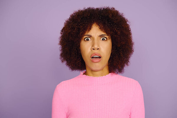 Молодая женщина с вьющимися волосами показывает взгляд шока во время ношения случайный розовый наряд против фиолетового.