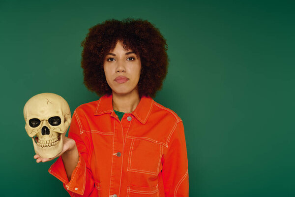 A pretty young woman expresses her emotions, holding a skull with a striking green background surrounding her.
