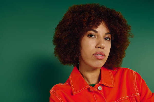 A young African American woman in casual attire expresses her emotions powerfully, set against lush green.