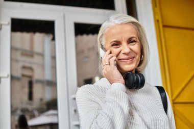 Neşeli, olgun bir kadın, güneşli bir günün tadını çıkarırken telefonundan sıcacık bir şekilde sohbet ediyor..