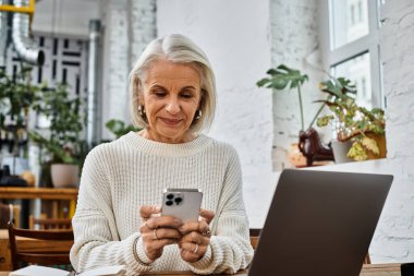 Güzel, olgun bir kadın bir kafede akıllı telefonuyla iletişim kurar. Teknoloji ve rahatlama ile harmanlanır..