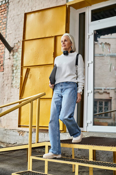 A stylish woman with gray hair walks gracefully, showcasing her fashion near a lively doorway.