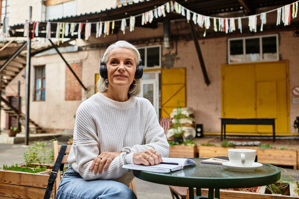 A mature beautiful woman relaxes with coffee and headphones in a charming courtyard setting.