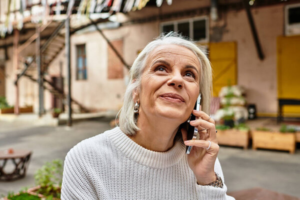 A mature woman with elegant gray hair enjoys a phone conversation in a vibrant outdoor space.