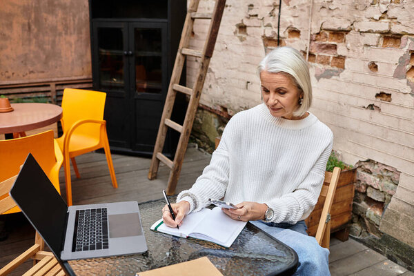 Задумчивая женщина с седыми волосами наслаждается записью в блокноте на очаровательном открытом воздухе.