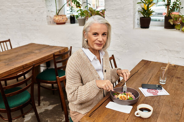 A graceful woman with gray hair savors a delicious bowl of food at a charming cafe.