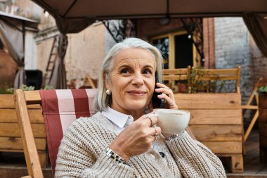 Gri saçlı güzel kadın kahvesini yudumluyor ve büyüleyici bir kafede rahatça sohbet ediyor..