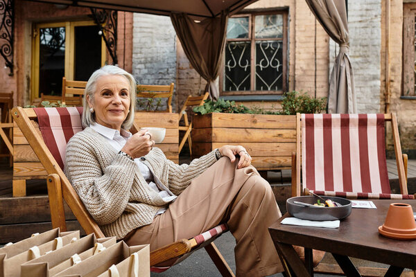 Прекрасная пожилая женщина наслаждается кофе в уютном открытом кафе, купаясь в теплом солнечном свете.