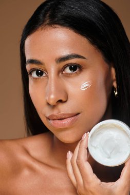 African American woman demonstrates skincare application with a cream in studio light. clipart