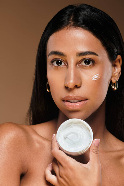 Женщина демонстрирует свою рутину по уходу за кожей со сливками в профессиональной студии.