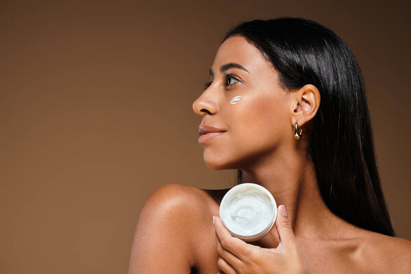Женщина наносит крем на щеку, подчеркивая красоту и уход за собой в студии.