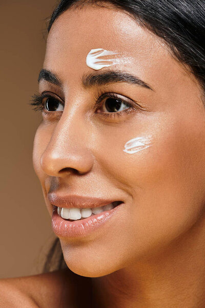 Женщина с брюнетками демонстрирует технику ухода за кожей, улыбаясь в студии.