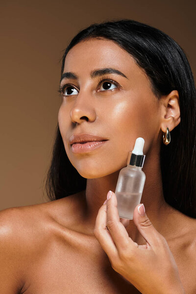 Уверенная в себе женщина демонстрирует свои привычки по уходу за кожей, держа в руках бутылку с сывороткой.