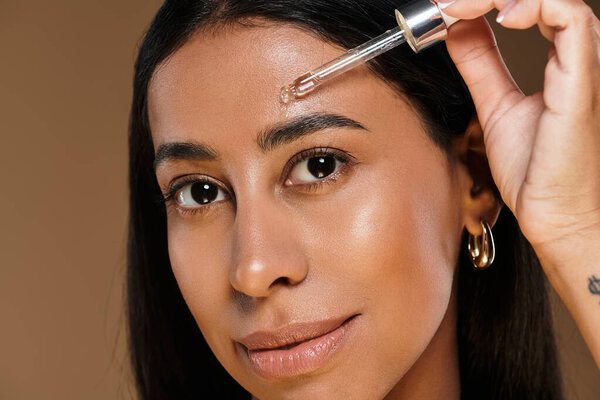 Женщина демонстрирует свои привычки к уходу за кожей, нанося сыворотку на лоб в студии.