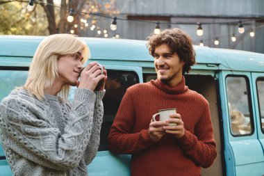 Büyüleyici bir açık hava ortamında, genç ve sevecen eşcinsel çift eski bir minibüsün yanında kupalarını yudumlarken kahkahalar ve sıcaklığı paylaşıyor. Samimi kazakları dost atmosferi vurguluyor..