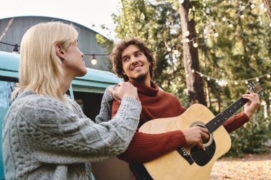 Genç ve sevecen eşcinsel çift, biri gitar çalarken diğerinin dikkatle izlediği neşeli bir anı paylaşıyor..