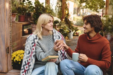 Amidst a colorful garden, two young friends enjoy each others company on a pleasant autumn afternoon. They share warm drinks, laughter, and a cozy blanket, surrounded by blooming flowers. clipart