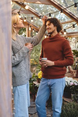 In a serene garden filled with vibrant flowers, a young couple shares a joyful moment. The warm glow of string lights enhances the cozy atmosphere as they smile at each other, creating a loving scene. clipart