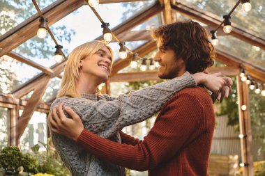 Young loving gay couple share a joyful moment in a beautiful greenhouse filled with greenery. clipart