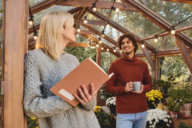 In a serene greenhouse filled with vibrant plants, Young loving gay couple share a warm conversation. One holds a book, while the other enjoys a steaming cup, both radiating joy and charm. clipart