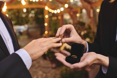 In a romantic garden adorned with twinkling lights, two young men exchange wedding rings, embracing their love. The moment captures joy, commitment, and the magic of LGBTQ celebration. clipart